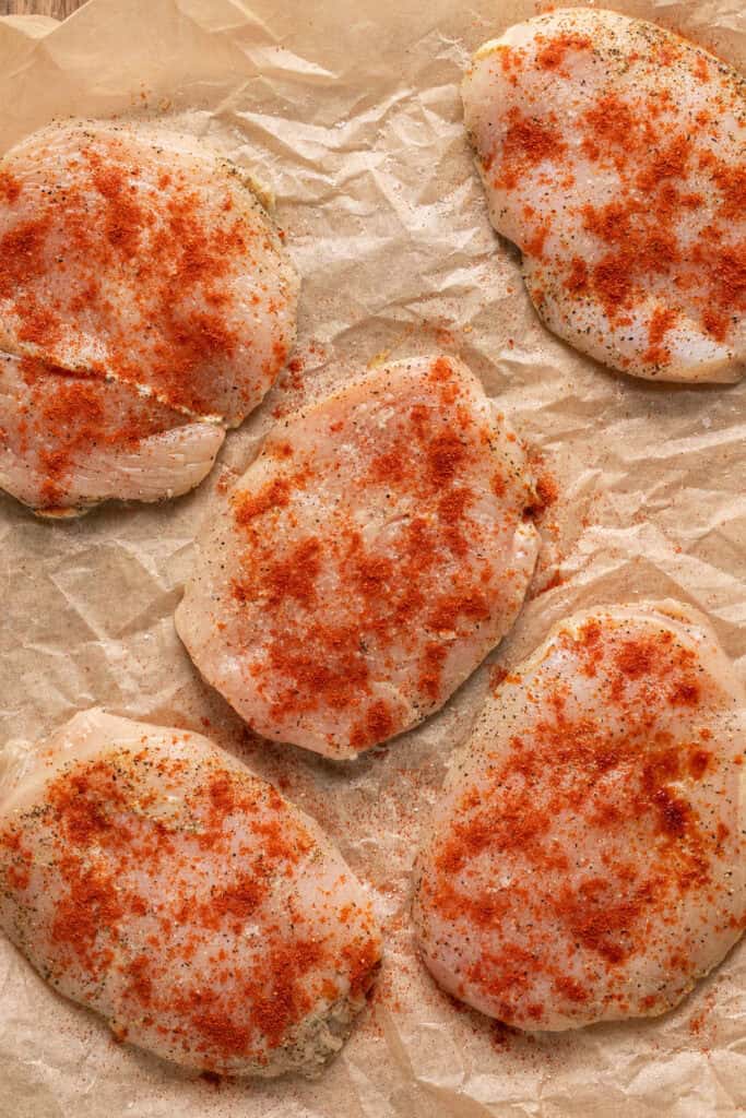 Raw chicken breasts on parchment paper sprinkled with paprika.