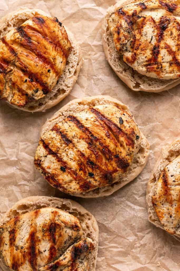 The bottom half of english muffins topped with cooked chicken breasts.