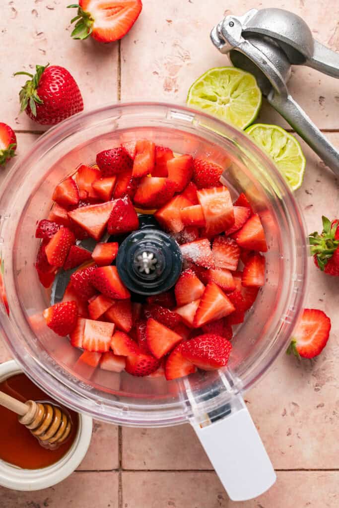 Sliced strawberries in a food processor bowl before being processed.