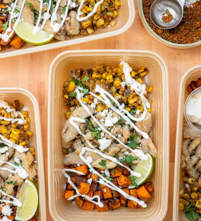 Mexican Street Corn Chicken Bowls drizzled with sour cream in meal prep containers.