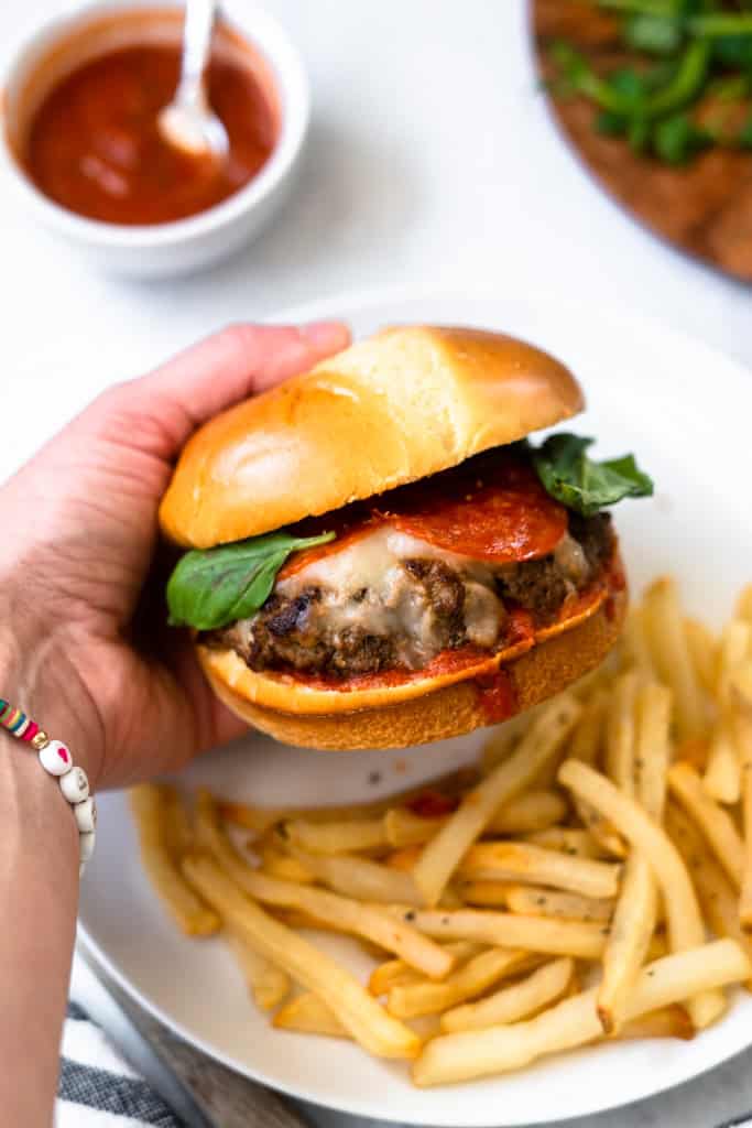 A hold holding a pizza burger with fries on a plate in the background.