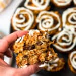 A hand holding a Carrot Cake Baked Oat Cup with a tray of Carrot Cake Baked Oat Cups in the background.