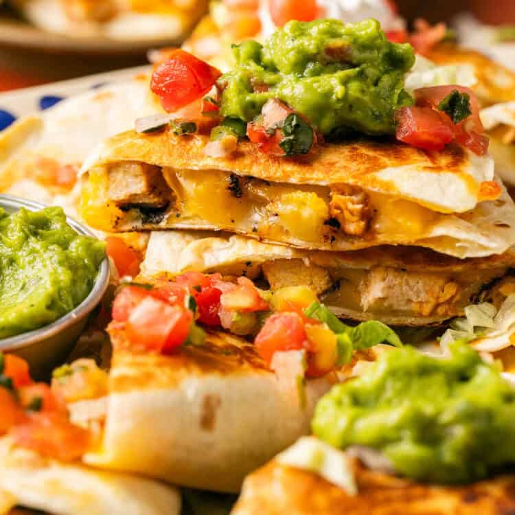 Grilled Chicken Quesadillas topped with guacamole, sour cream, and pico de gallo on a platter.