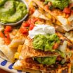 Zoomed in view of Grilled Chicken Quesadillas topped with guacamole, sour cream, and pico de gallo on a platter.