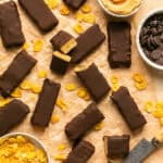 Chocolate peanut butter protein bars on parchment paper with small bowls of chocolate chips and corn flakes.