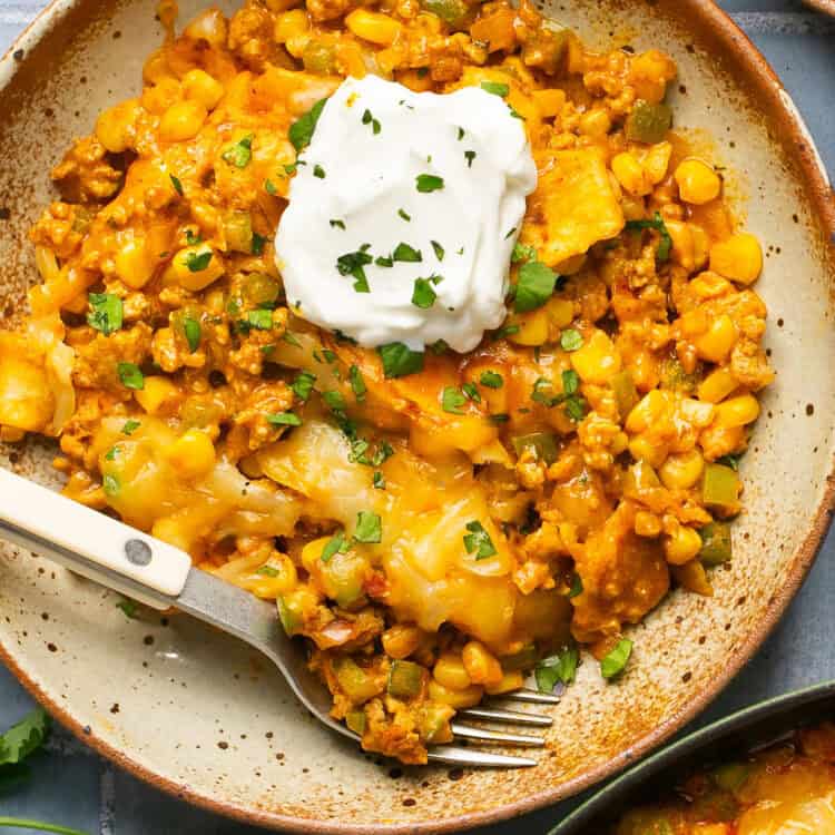 Elote Ground Turkey Skillet topped with sour cream on a plate with a fork.