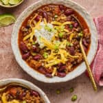 Classic Beef & Bean Chili topped with shredded cheese, green onion, and sour cream in bowls.