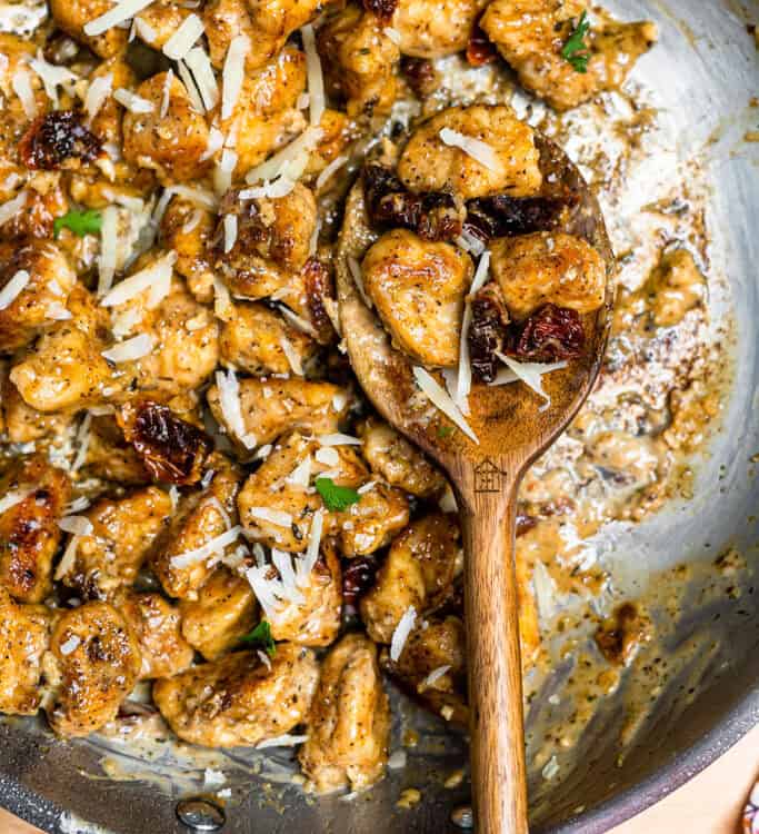 Marry me chicken bites in a skillet with a wooden spoon.