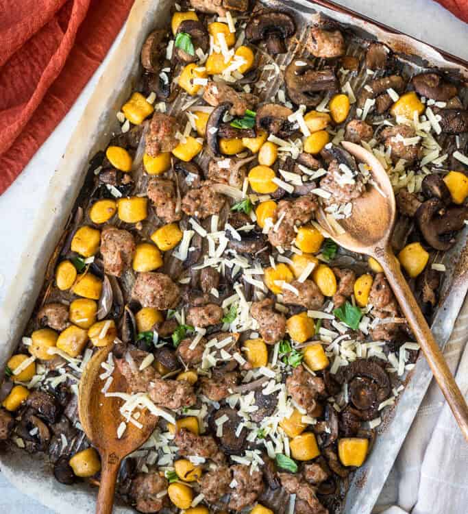 Sheet pan sausage and gnocchi on a sheet pan with wooden spoons.