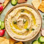 White Bean Dip in a small bowl garnished with crackers, radishes, and cucumbers.