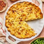 Quiche Lorraine in a round baking dish with one slice missing.