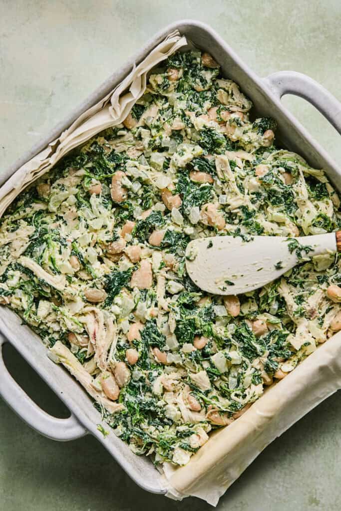 Chickend and spinach mixture being added to the phyllo sheets in a square baking dish.