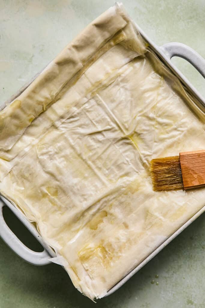 Phyllo sheets placed on top of the chicken and spinach mixture and being brushed with oil.