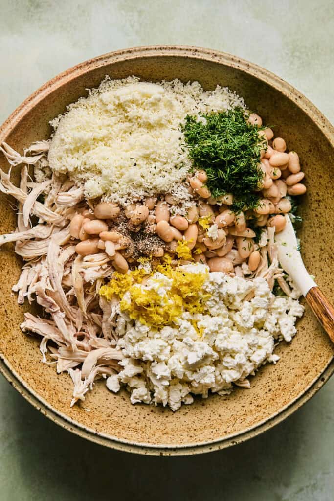 Beans, chicken, feta, parmesan, dill, lemon zest, and pepper added to the spinach mixture in a bowl.
