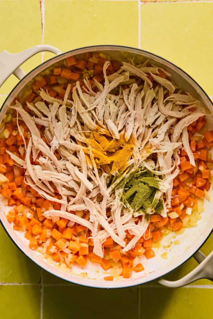 Cooked shredded chicken and seasonings added to the chopped veggies in a dutch oven.