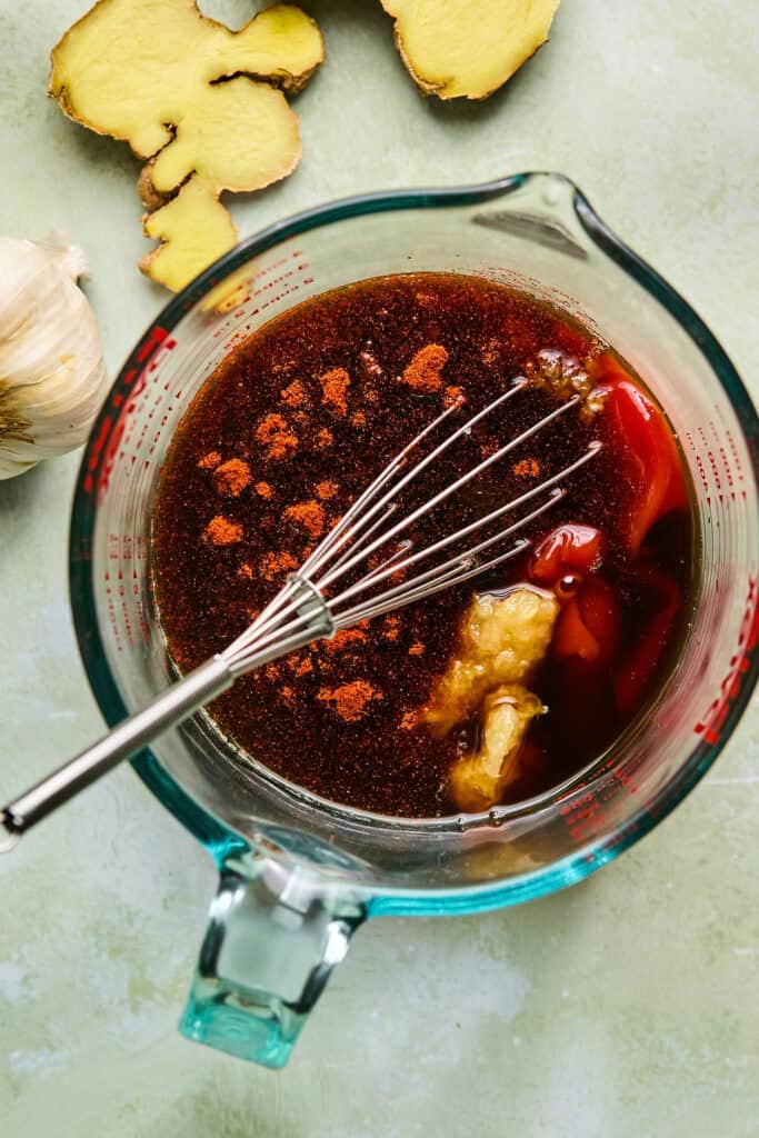 Marinade ingredients in a glass measuring cup with a whisk.