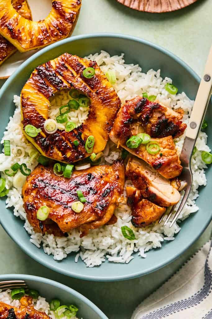 Huli Huli Chicken with pineapple rings over rice in a bowl with a fork.