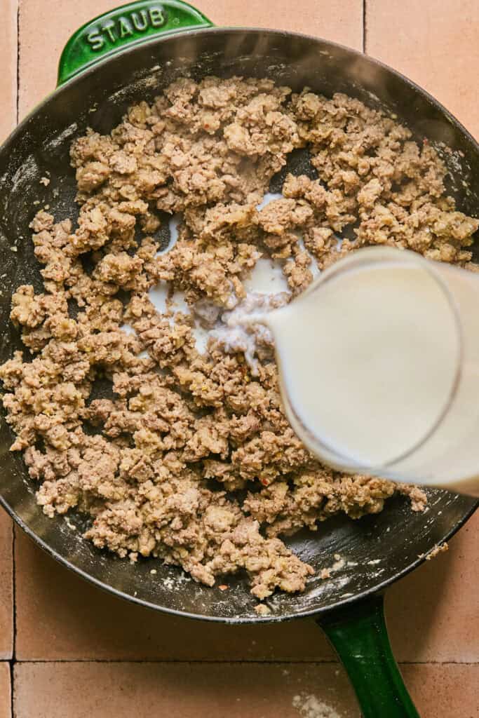 Milk being added to the skillet of cooked turkey sausage.