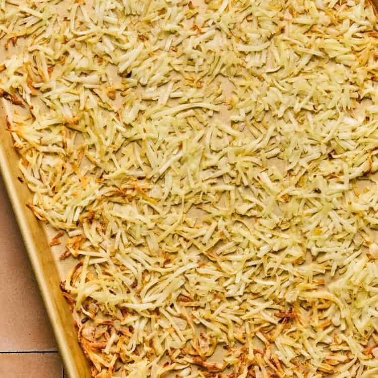 Hashbrowns spread out on a baking sheet after being browned.