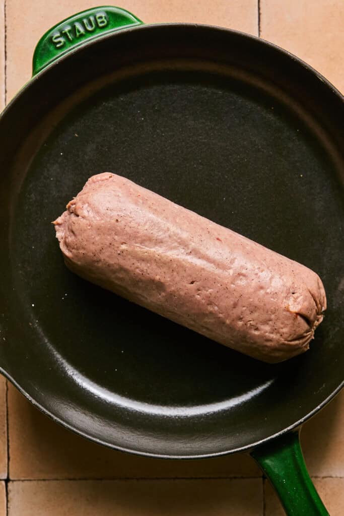 Roll of raw turkey sausage in a skillet.