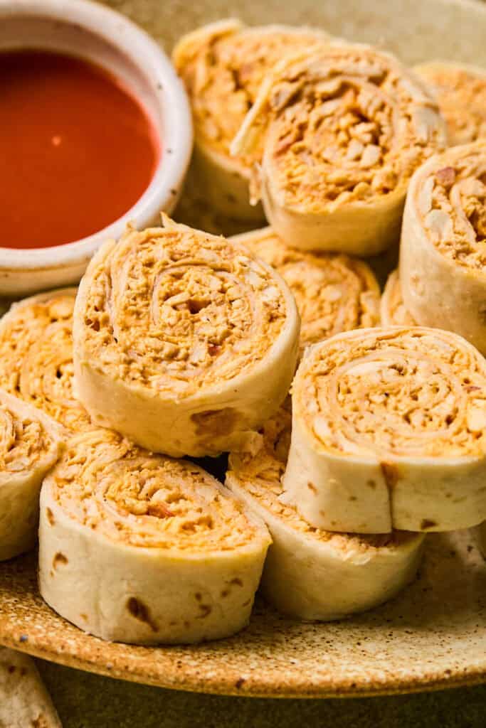 Buffalo Chicken Pinwheels in a tray with a side of buffalo sauce.