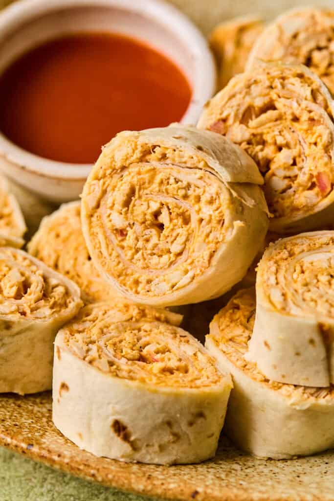Zoomed in view of Buffalo Chicken Pinwheels on parchment paper with a side of buffalo sauce.