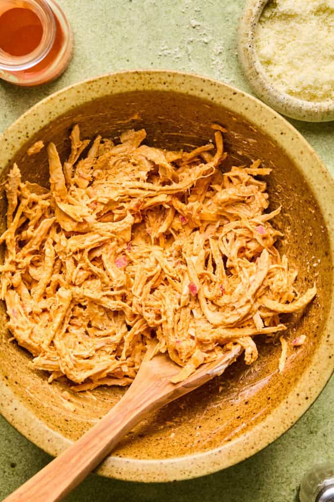 Buffalo chicken in a bowl with a wooden spoon.