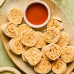 Buffalo Chicken Pinwheels on a tray with a side of buffalo sauce.