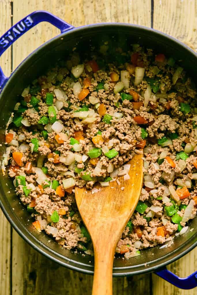 Ground beef and veggies cooking in a pot with a wooden spoon.