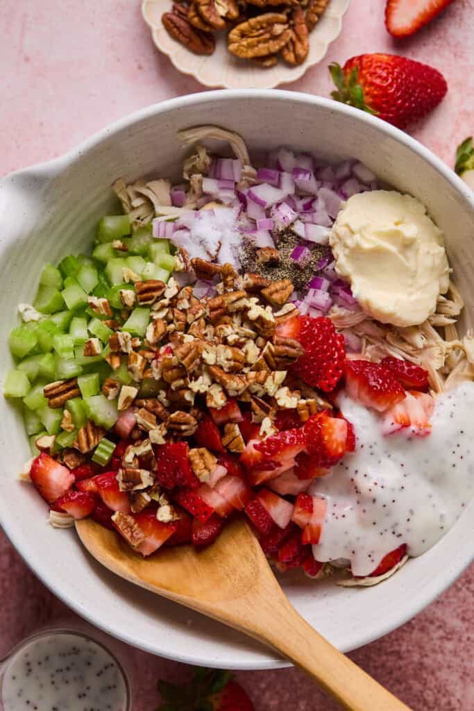 Ingredients for Strawberry Poppyseed Chicken Salad in a mixing bowl with a wooden spoon.