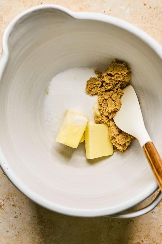 Butter, brown sugar, and sugar in a mixing bowl with a spatula.