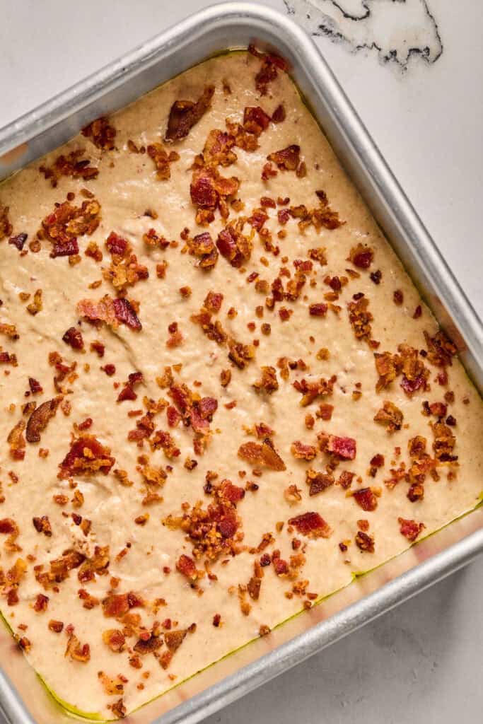 Bacon crumbles on top of the Maple Bacon Pancake Bake batter in a baking dish.