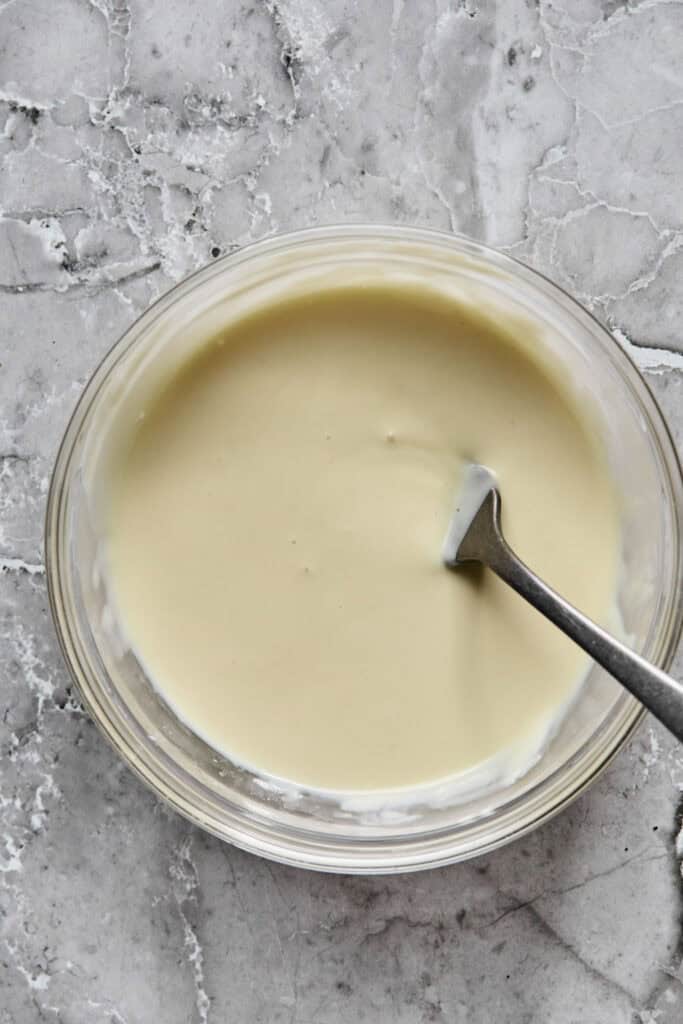 Melted white chocolate in a bowl with a spoon.