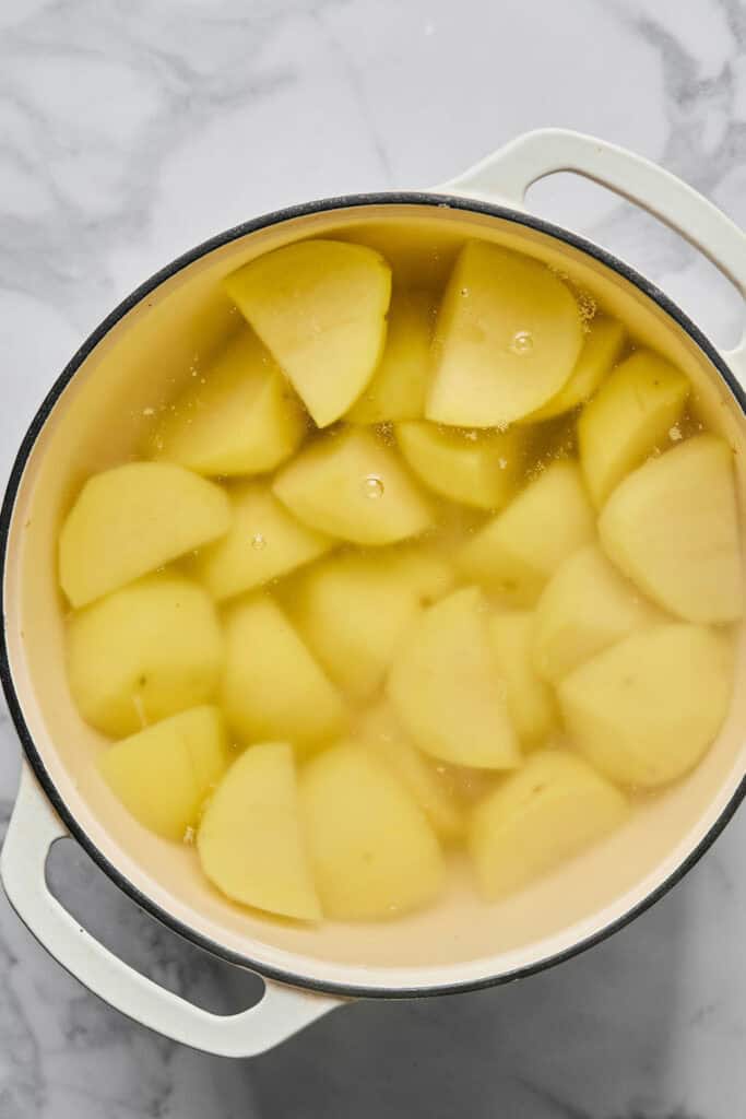 Peel and quartered potatoes in water in a pot.