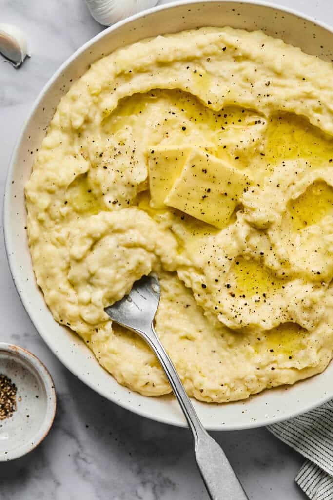 Garlic Mashed Potatoes topped with butter in a bowl with a spoon.