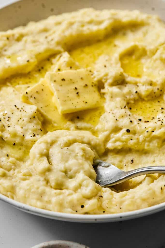 Zoomed in view of garlic mashed potatoes topped with butter in a bowl with a spoon.