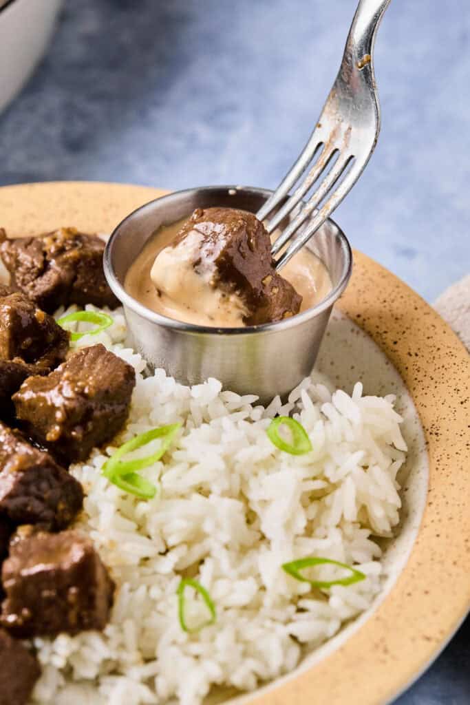 Hibachi Steak being dipped in yum yum sauce and a plate with more Hibachi Steak and rice.