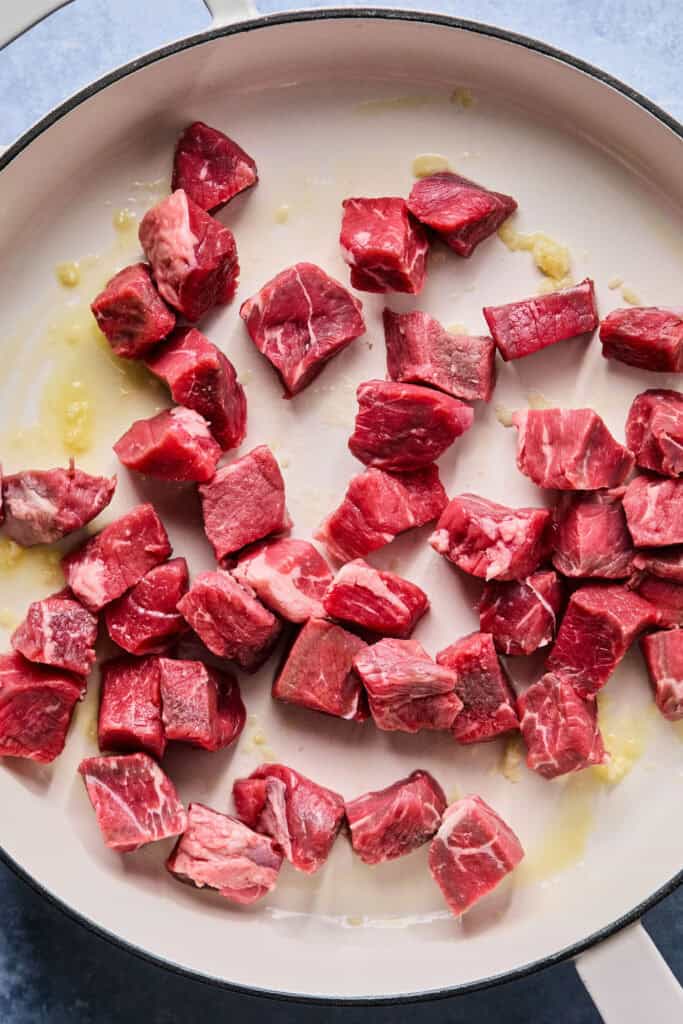 Uncooked steak bites in a skillet.