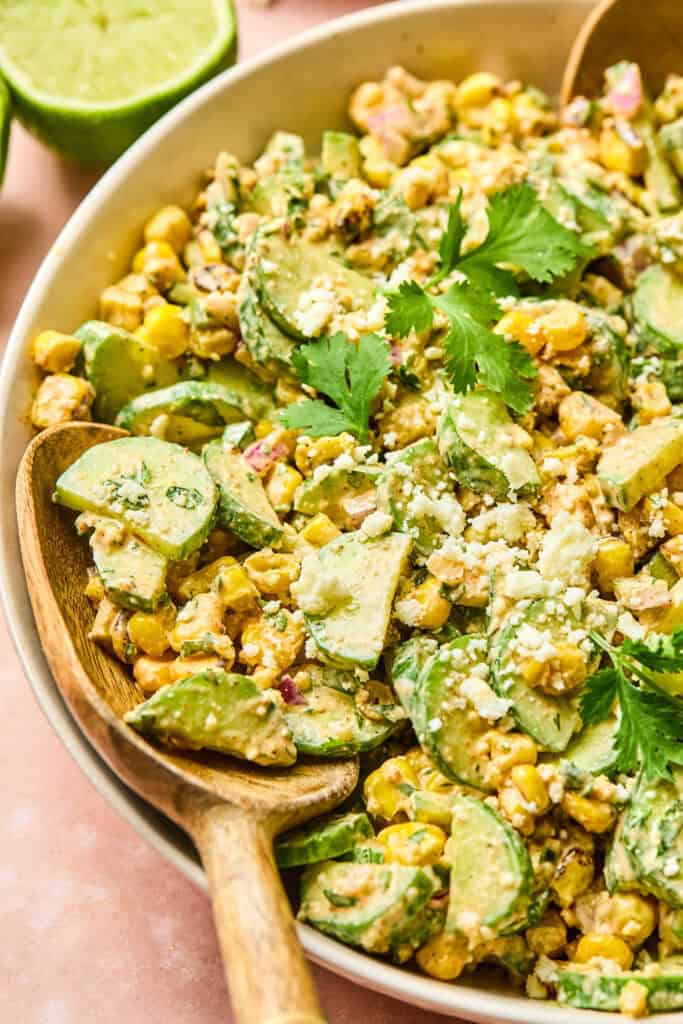 Mexican Cucumber Corn Salad in a large bowl with a wooden spoon.