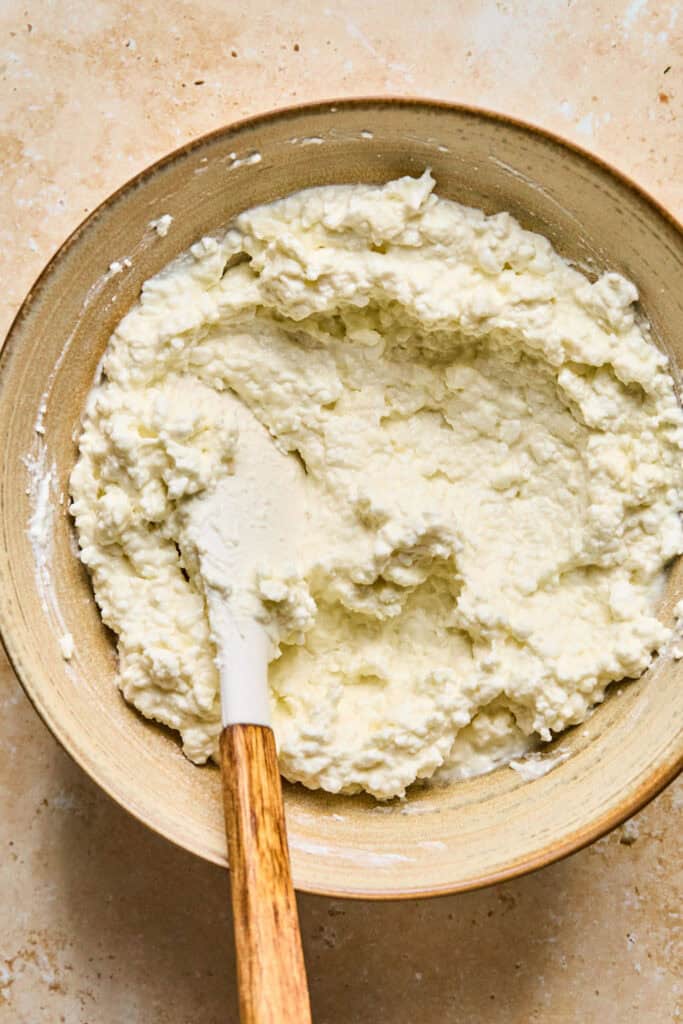 Softened cream cheese in a bowl with a wooden spoon.