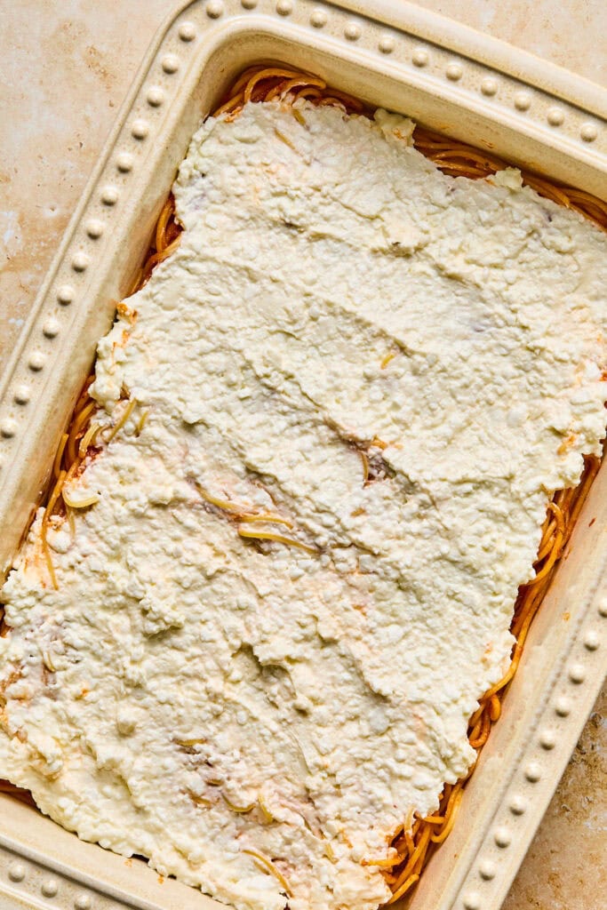 Cream cheese spread over the spaghetti in a baking dish.
