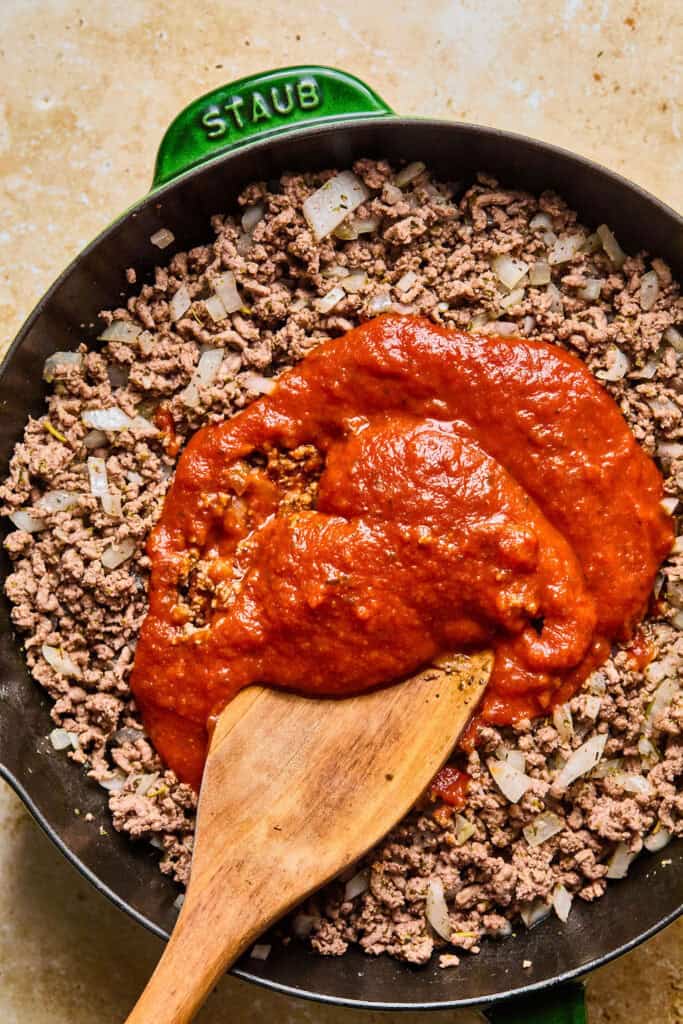 Cooked ground beef topped with tomato sauce in a skillet,