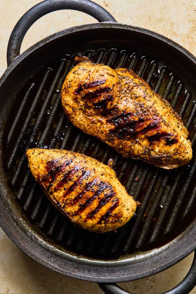 Two charred chicken breasts in a grill pan.