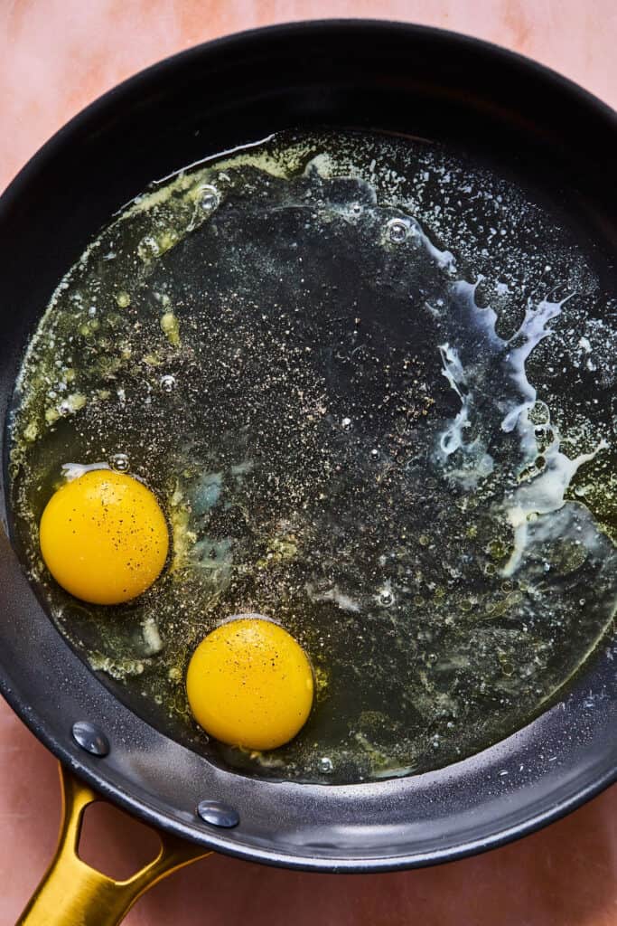 Teo eggs in a skillet with melted butter.