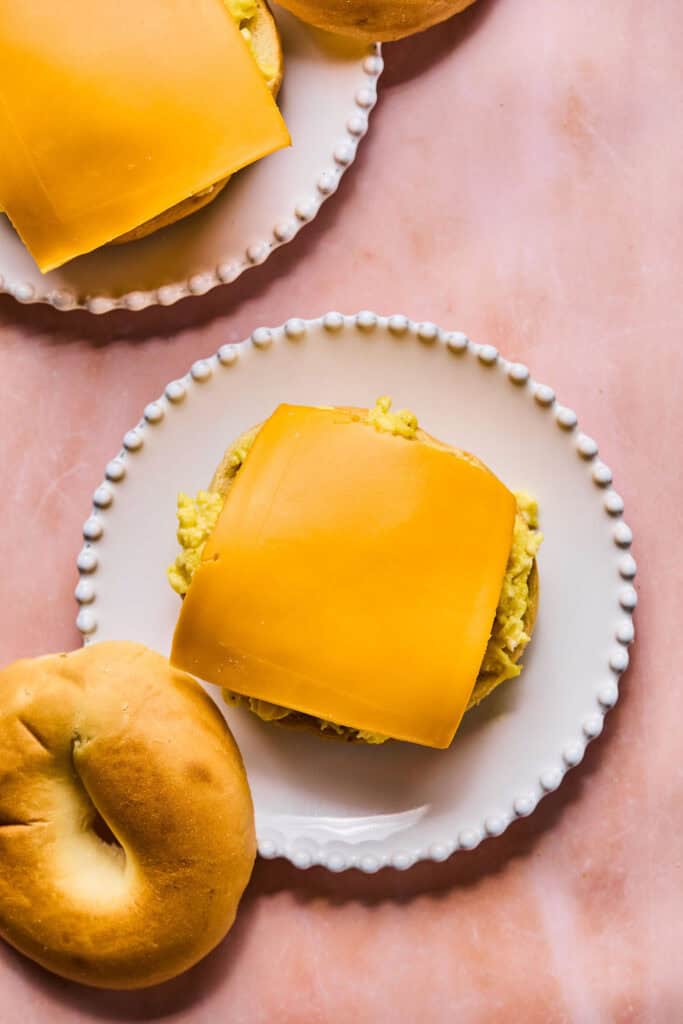 A slice of cheese on top of eggs and a bagel on a small plate.