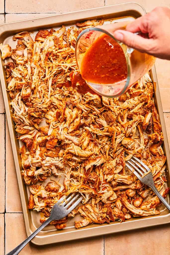 Sauce being poured over the Honey Chipotle Chicken on a baking sheet.