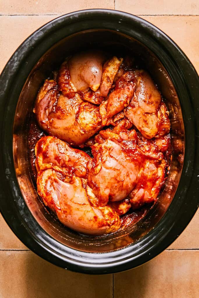 Raw chicken thighs in Honey Chipotle sauce in a slow cooker bowl.