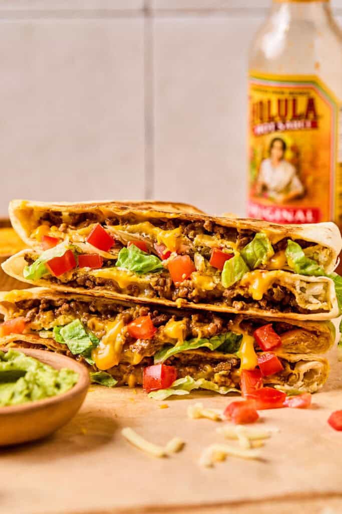 Crunchwrap Supreme cut in half and stacked on top of each other with a side of guacomole.