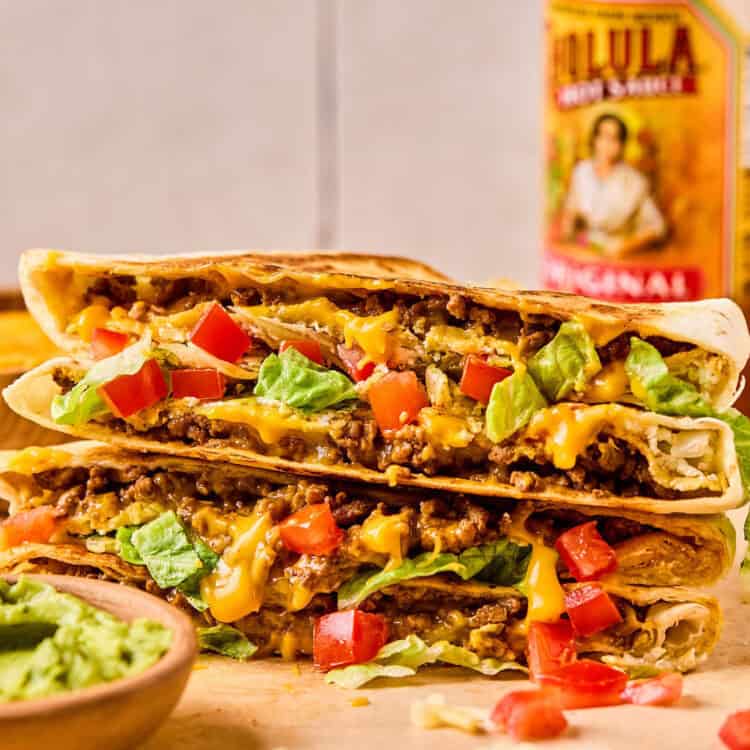 Crunchwrap Supreme cut in half and stacked on top of each other with a side of guacomole.