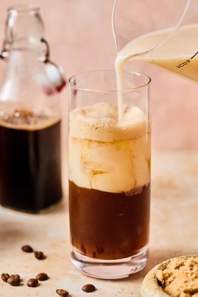 Milk being poured in the the tall glass with the espresso mixture.